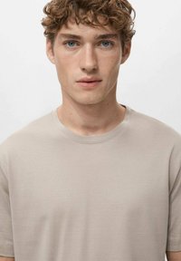 Lys beige kortærmet t-shirt lavet af glat stof, med rund hals og en afslappet pasform, synlige syninger på ærmerne.