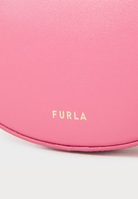 Rózsaszín bőrből készült kerek táska sima felülettel, az alján aranyszínű "FURLA" logó felirattal. Nincs látható hardware.