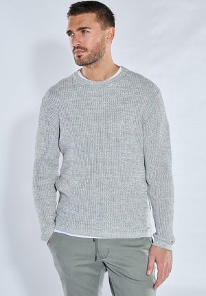 Gray knitted sweater with a textured pattern, featuring a round neckline and long sleeves, layered over a white T-shirt, paired with gray trousers.