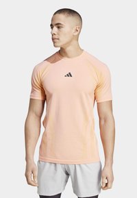 Camisa deportiva de manga corta en rosa claro, con un logo negro y acentos texturizados a lo largo de los lados para una mejor transpirabilidad.