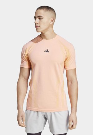 T-shirt de sport à manches courtes en rose clair, avec un logo noir et des accents texturés sur les côtés pour une meilleure respirabilité.