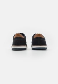 Baskets noires avec des accents en cuir marron, présentant un design bas, un bout arrondi, des coutures contrastantes et une semelle en caoutchouc blanche.