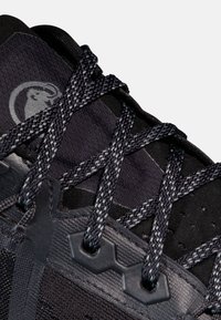 Schwarzer Sportschuh mit strukturiertem Obermaterial, gewebten Schnürsenkeln und geometrischen Akzenten. Logo auf der Seite geprägt, dezenter Glanz auf dem Material.