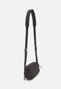 Černá crossbody taška vyrobená z hladké kůže, s elegantním obdélníkovým tvarem, nastavitelným popruhem a modrým zipem.