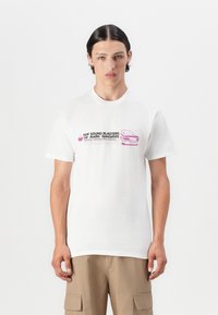 Hvit bomulls T-skjorte med grafisk trykk i rosa og svart, som viser teksten "HUF SOUND BLASTERS" og en illustrasjon av en bil.