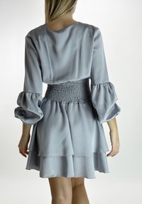 Abito grigio chiaro con vita arricciata, maniche lunghe a palloncino e orlo a strati con volant. Texture liscia simile al satin, design semplice ed elegante.