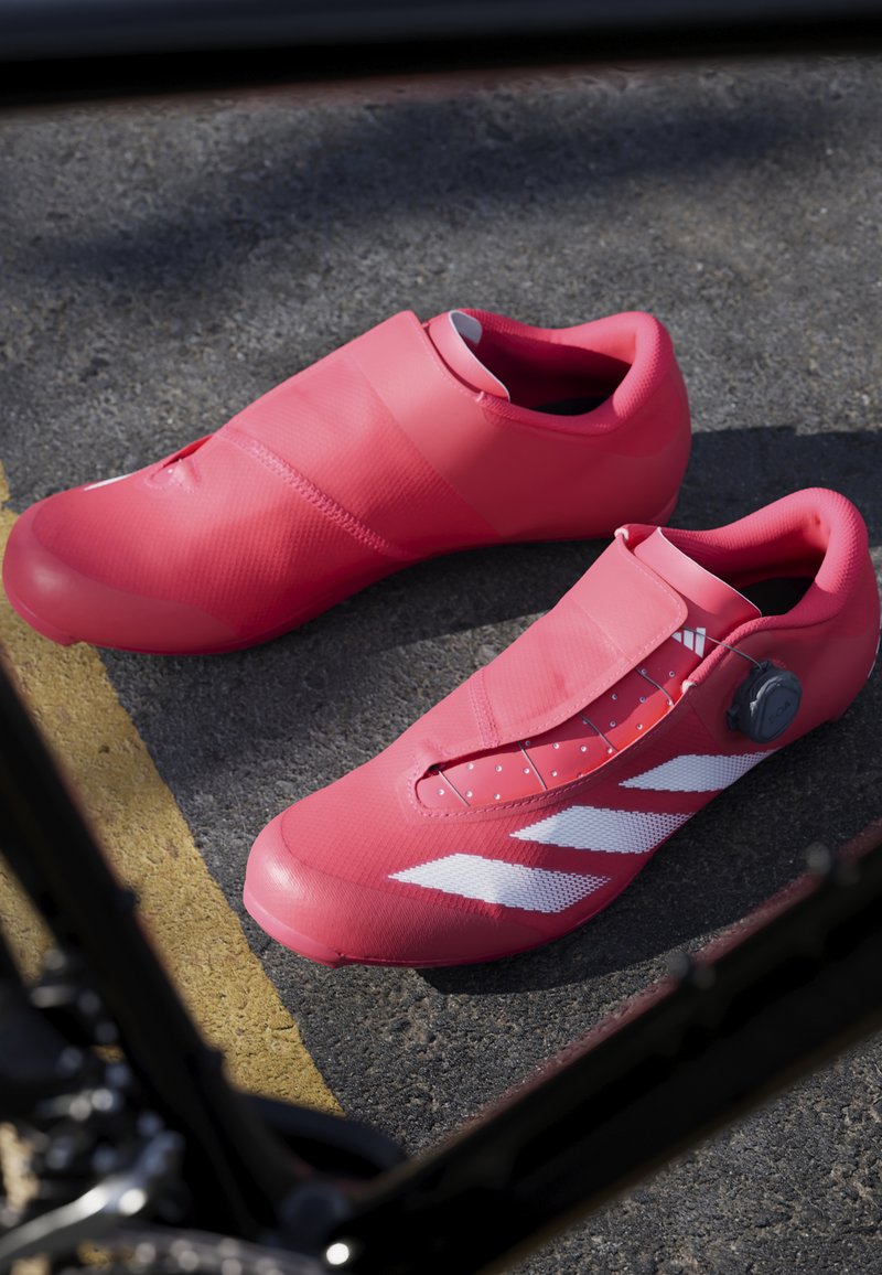 Rosa Fahrradschuhe verfügen über ein glattes Synthetik-Obermaterial mit einem Klettverschluss und einer Drehverschlussvorrichtung. Auffällige weiße Streifen und durchbrochene Details verbessern das Design.