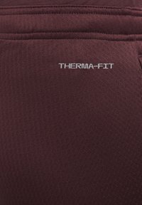 Maroonowa tkanina Therma-Fit o teksturowanej powierzchni z subtelnym geometrycznym wzorem. Na boku widoczne jest srebrne logo.