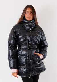 Giacca piumino nera e lucida con collo alto, chiusura frontale con zip e vita cintata. Presenta cuciture a zigzag e dettagli rosa sui polsini.