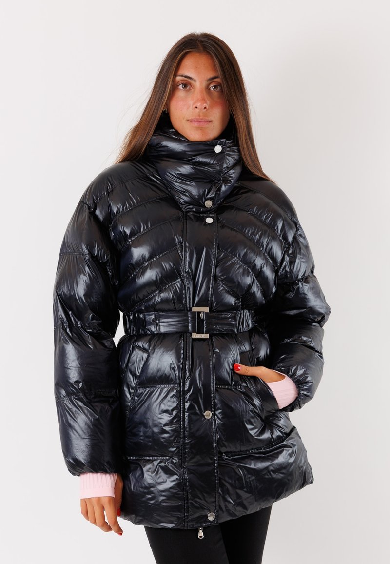 Giacca piumino nera e lucida con collo alto, chiusura frontale con zip e vita cintata. Presenta cuciture a zigzag e dettagli rosa sui polsini.