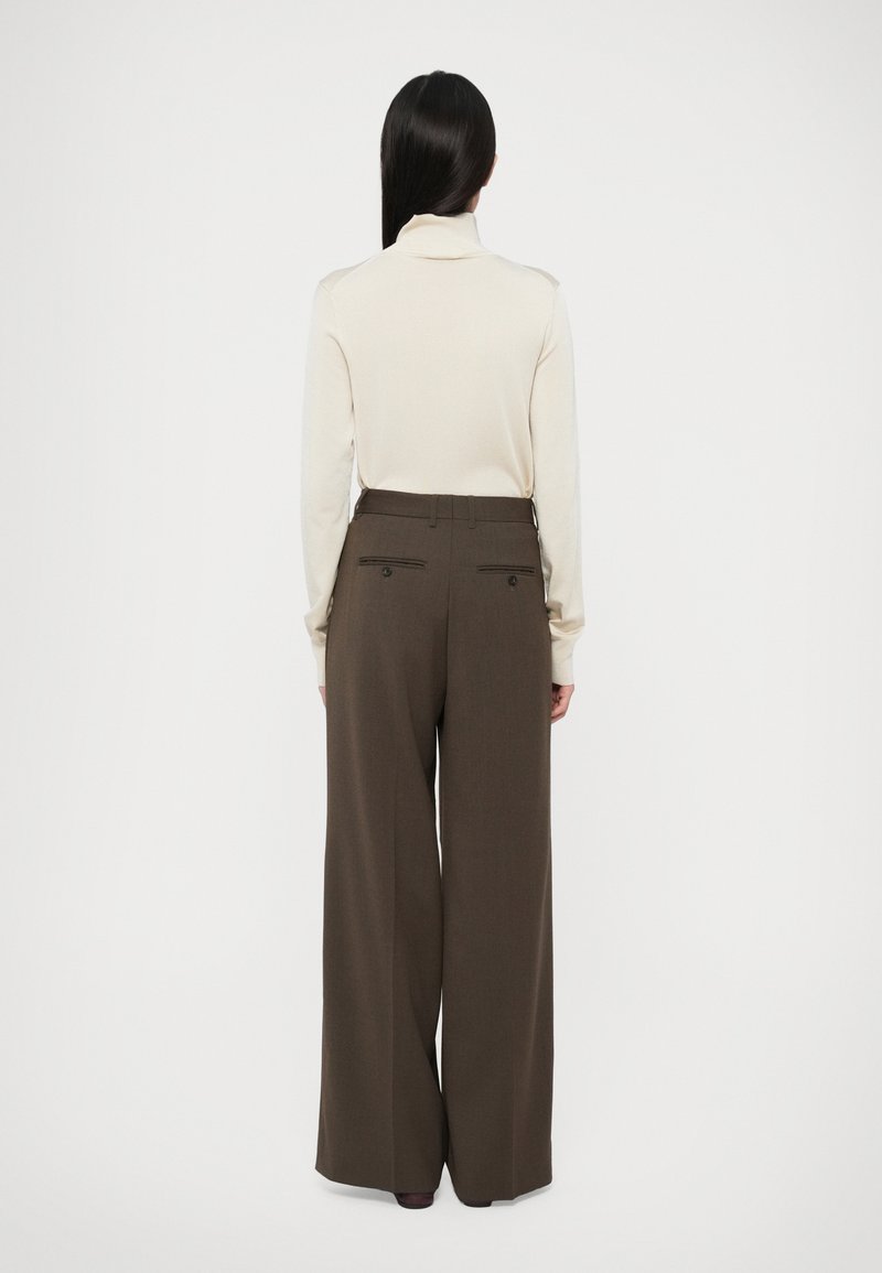 Light beige turtleneck sweater and wide-leg dark brown trousers with rear pockets and button accents. Smooth texture and tailored fit.