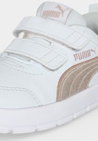 Λευκό αθλητικό παπούτσι Puma με δύο λουράκια βέλκρο, μπεζ πλευρική ρίγα από σουέντ και λογότυπο Puma στη γλώσσα και την πλευρά.