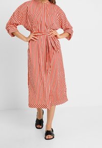 Midi-kjole med røde og hvide striber, korte ærmer, bælte i taljen og to forlommer. Bærtes med sorte slip-on sandaler.