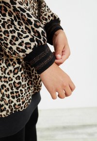 Maglione con stampa leopardata, dotato di polsini a coste neri e metallici, caratterizzato da una texture del tessuto morbida e un design ampio.