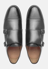 Chaussures en cuir noir avec une finition lisse, dotées de deux fermetures à boucle en métal argenté et d'un embout rond. L'intérieur est en cuir beige clair.