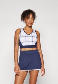 Marine atletisk crop top med hvit rutemønster og merket svart midjebånd, kombinert med et marineblått skjørt med hvite detaljer.