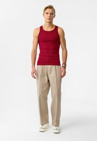 Rode geribbelde tanktop, beige geplooide broek en witte sneakers. De outfit heeft een relaxte pasvorm en gladde texturen.