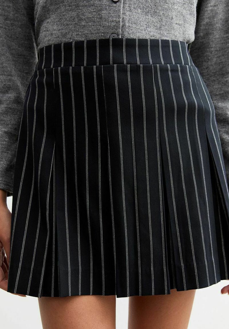 Falda negra con pliegues que presenta rayas verticales blancas, confeccionada en una tela suave con una cinturilla estructurada. Diseñada para un ajuste entallado.