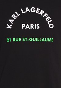Černé tričko s bílým a zeleným textem: "KARL LAGERFELD PARIS 21 RUE ST-GUILLAUME" s tučnou, moderní typografií.