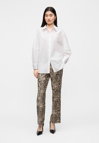 Άσπρο πουκάμισο με μακριά μανίκια, γιακά με κουμπιά και διακοσμητικές τρύπες, συνδυασμένο με παντελόνι λεοπάρ. Το μοντέλο φοράει μαύρες μυτερές ψηλοτάκουνες γόβες.