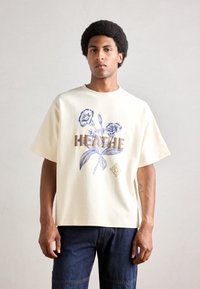 Krystalklar oversized t-shirt i cremefarvet bomuld, med blåt blomsterprint og teksten "BREATHE". Korte ærmer og en afslappet pasform.