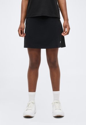 Person wearing a black skirt, white socks, and white sneakers, standing against a plain light background.
