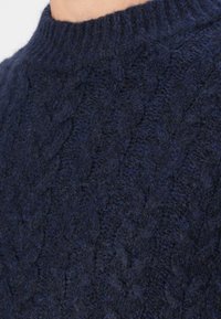 Suéter de punto cable en azul marino con cuello alto, hecho de un material texturizado y suave. Presenta un grueso cuello acanalado.