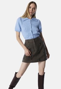 Lichtblauwe cardigan met korte mouwen, kraag en knoopsluiting, gecombineerd met een bruine geruite minirok met geborduurde accenten en zakken.