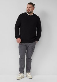 Zwarte geribbelde gebreide trui met een ronde hals, gecombineerd met grijze cargobroek met meerdere zakken en beige sneakers.