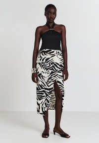 Schwarzes Neckholder-Top kombiniert mit einem knielangen weißen Rock, der ein auffälliges schwarzes Zebra-Muster und einen hohen Schlitz hat. Elegante schwarze Sandalen.