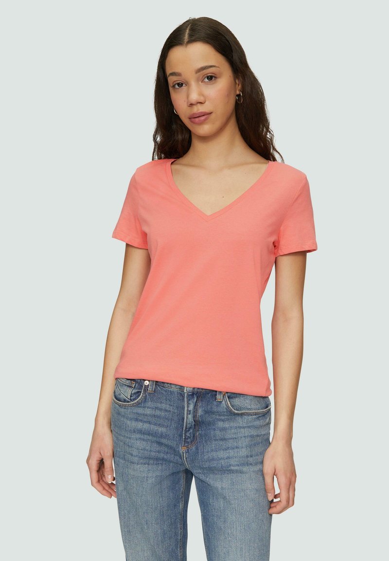 Koralowa koszulka z krótkim rękawem i dekoltem w serek, wykonana z gładkiej bawełny. Noszona z niebieskimi dżinsami, ma swobodny i komfortowy krój.