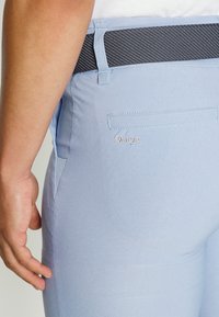 Helleblaue Hose mit glatter Textur, ausgestattet mit einem schwarzen Mesh-Bund und einem gestickten "Daily"-Logo nahe der Gesäßtasche.