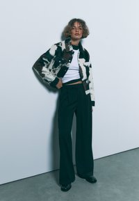 Nabrana jakna s kravjim vzorcem in mehko teksturo, v črno-belem barvnem spektru. Kombinirana z visokim pasom črnimi hlačami in sijočimi čevlji.