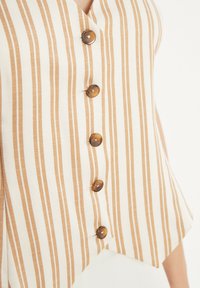 Gestreifter ärmelloser Top in Creme und Beige, mit einem V-Ausschnitt und fünf runden braunen Knöpfen. Der Stoff hat eine glatte Textur und eine lockere Passform.