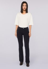 Bílé triko s krátkým rukávem v kombinaci s tmavými, přiléhavými kalhotami. Oblečení je jednoduché, má hladkou strukturu a klasický design.