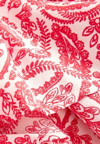 Röd och vit mönstrad tyg med blommiga och paisleymotiv, med en mjuk textur och en lätt, fallande kvalitet.