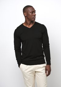 Svart v-ringad tröja i ribbad stickning, lång ärm, figurnära design, tillsammans med krämfärgade byxor, slät textur och minimalistisk stil.