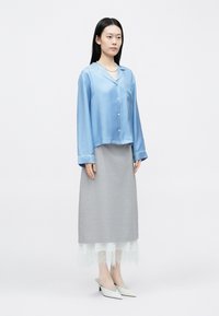 Világoskék szatén ing hosszú ujjakkal és gombokkal, szürke szoknyával, amely csipkés szegéllyel díszített. A szett fehér, hegyes orrú cipővel van kiegészítve.