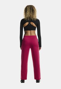 Zwarte lange mouw crop top met een open rug en kruislings straps, gecombineerd met hoge roze broek; gladde textuur, atletische fit.
