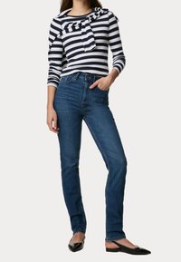 Top de manga larga a rayas con detalle de lazo, combinado con jeans azules. El top presenta rayas en azul marino y blanco; los jeans tienen un corte clásico y ajustado.