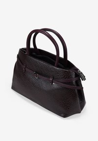 Bolso de mano de cuero en burdeos intenso con una superficie texturizada, que presenta dos asas y una parte superior con cremallera. Los acentos incluyen una delgada correa decorativa y una etiqueta.