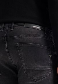 Zwarte denim jeans met een klassieke pasvorm, met een achterpatch met "PURE PATH" en een enkele achterzak met een gestreept accent.