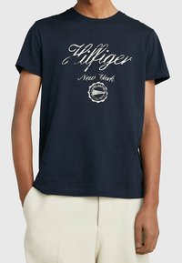 Marinblå bomullst-shirt med en vit logotypdesign som inkluderar "Hilfiger New York" och en cirkulär emblem i mitten. Kortärmad.