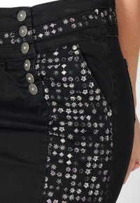 Črna denim krila z dekorativno vezenino v cvetličnih in diamantskih vzorcih. Zapiranje na pet gumbov z kovinskimi detajli in teksturirano površino.