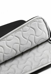 Custodia per laptop nera imbottita con interni grigi trapuntati a motivo ondulato, chiusa con una cerniera nera lungo il bordo.