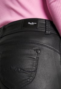 Mustat farkut ovat slim-fit -malliset, joissa on sileä pinta, näkyvät saumat ja merkattu musta nahkalappu vyötäröllä.