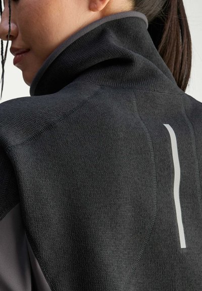 Maglione nero a maglia con colletto alto, caratterizzato da una finitura testurizzata. Una striscia bianca prominente accentua la parte posteriore.