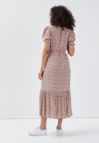 Vestido midi floral en tejido suave, con mangas abullonadas, cintura ajustada y dobladillo con volantes. El fondo es blanco liso. Combinado con zapatillas blancas.