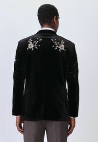 Black velvet blazer with floral embroidered details on the back and sleeves. Features a single vent and tailored fit.
