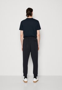 Svarta sweatpants med elastiska fållar, i kombination med en mörk t-shirt. Klädseln har en avslappnad passform och har en bakficka på byxorna.